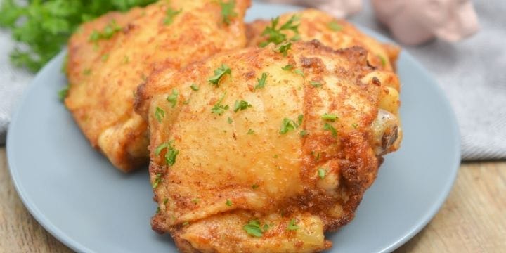 air fryer chicken thighs on a plate next to a towel, some parsley, and a piggie salt and pepper shakers