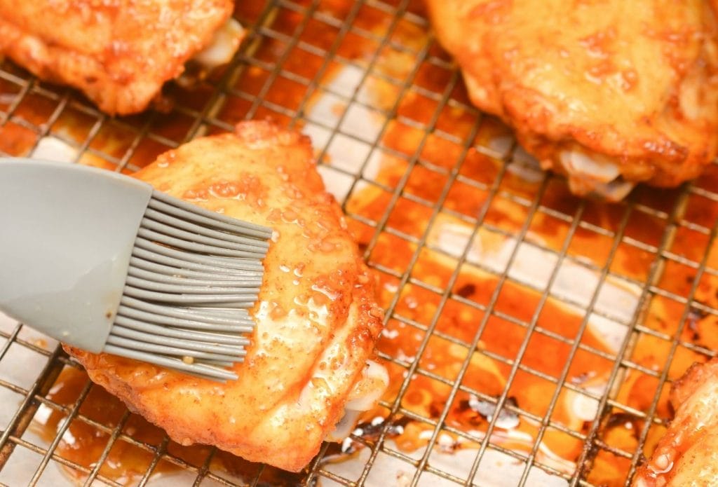 chicken thighs being brushed with sticky honey garlic sauce