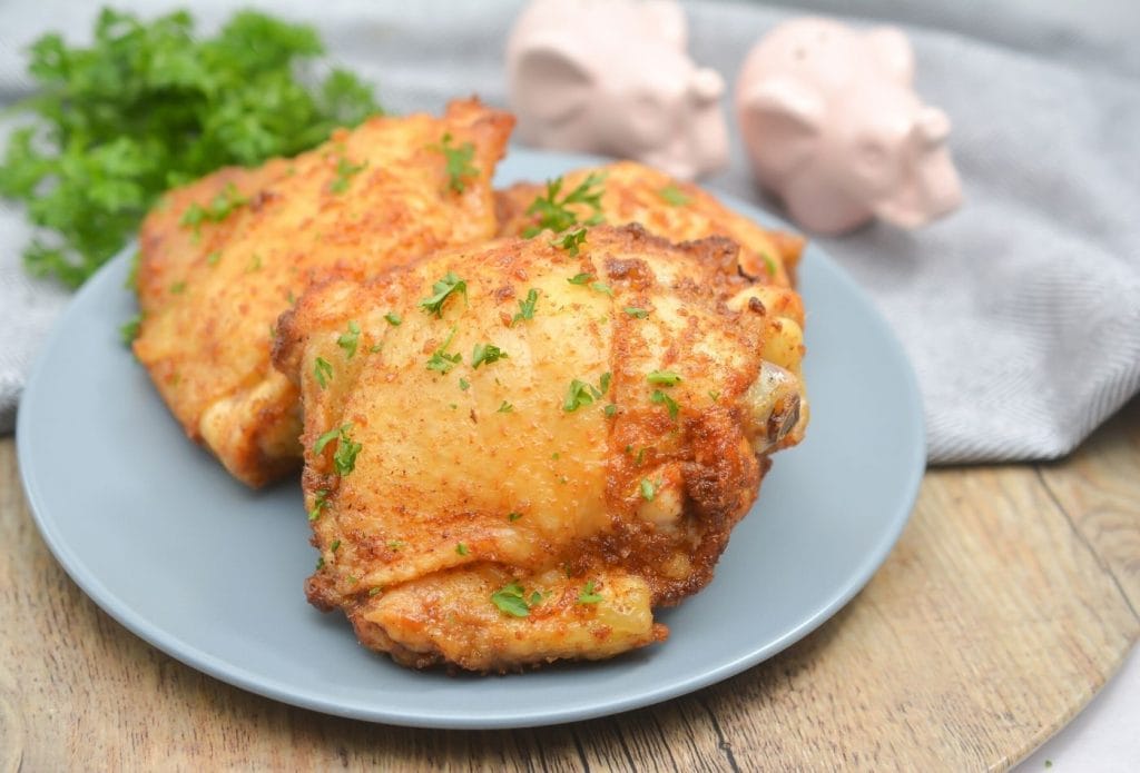 garlic honey ninja foodi chicken thighs on a plate on a board next to a towel and some elephant salt and pepper shakers that are white