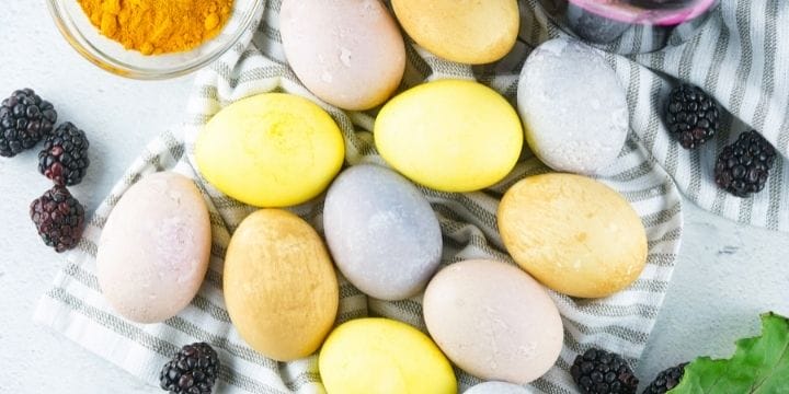 multi colored easter eggs on a towel with berries, beet juice, greens, and turmeric
