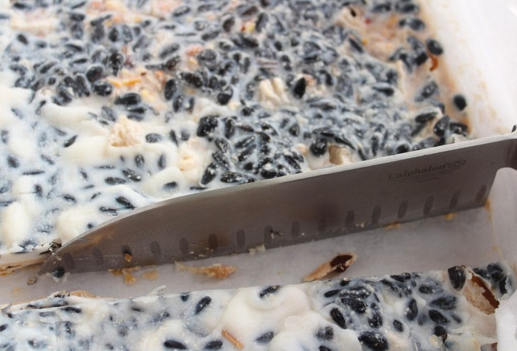 peanut butter pear bird suet cake in a pan being cut into squares with a knife