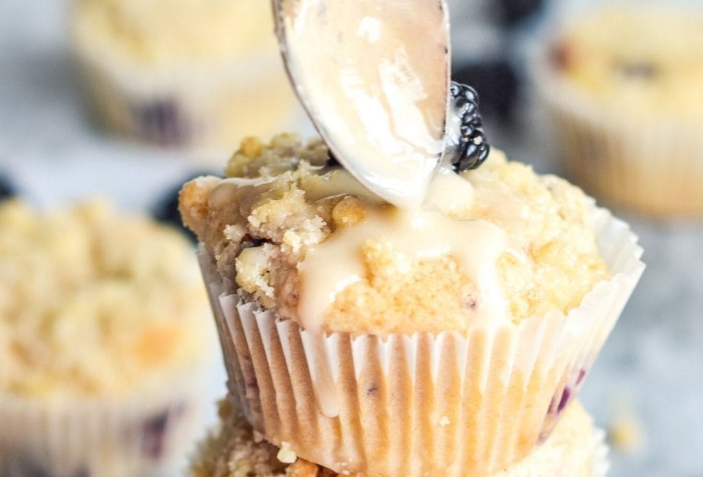 lemon drizzle being spooned onto a blackberry lemon crumb muffin