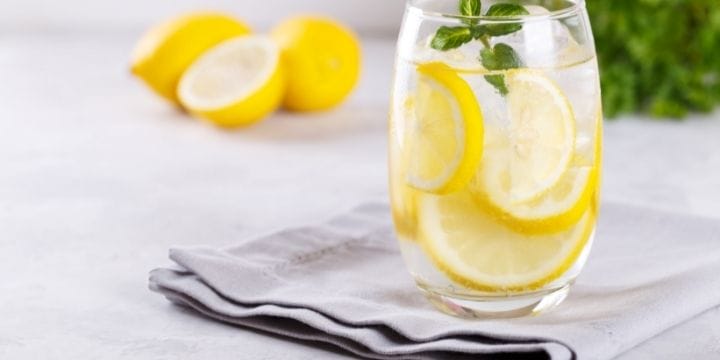 lemon infused water in a glass on a napkin garnished with herbs and with lemons behind it