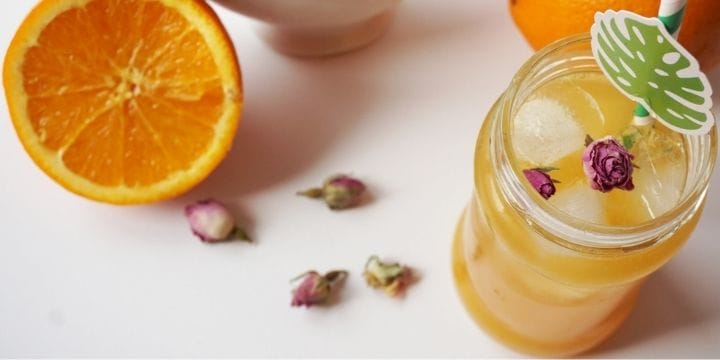 Tea, rose, and orange infused water on the counter with a sliced orange and dried roses