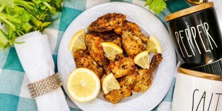 plate of crispy air fryer chicken wings with a napkin, fresh veggies, and salt and pepper shakers