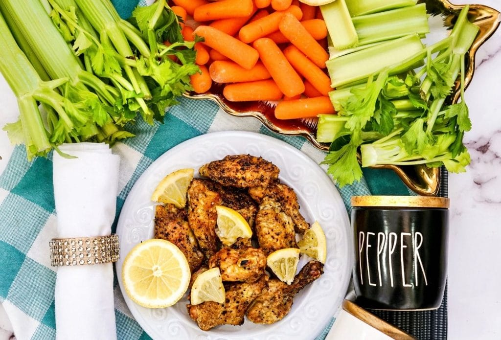 air fryer chicken wings on a plate with lemons and fresh carrots and celery