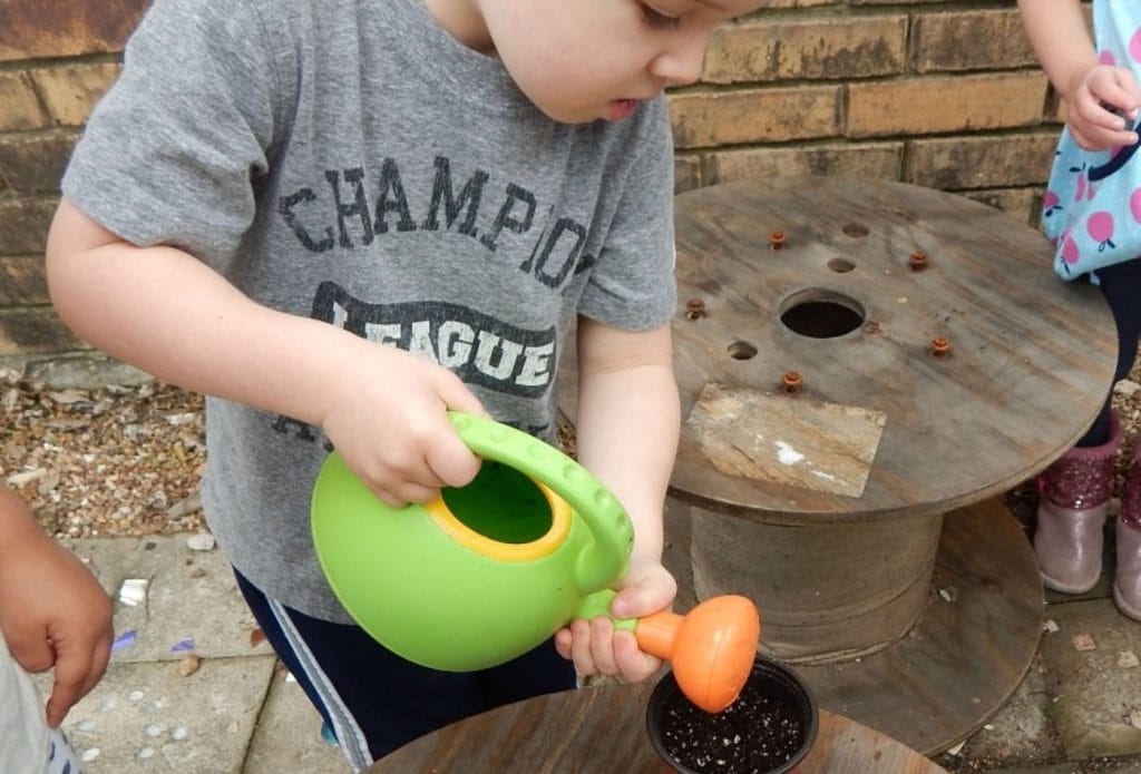 a young child watering a pot of seeds with a watering can