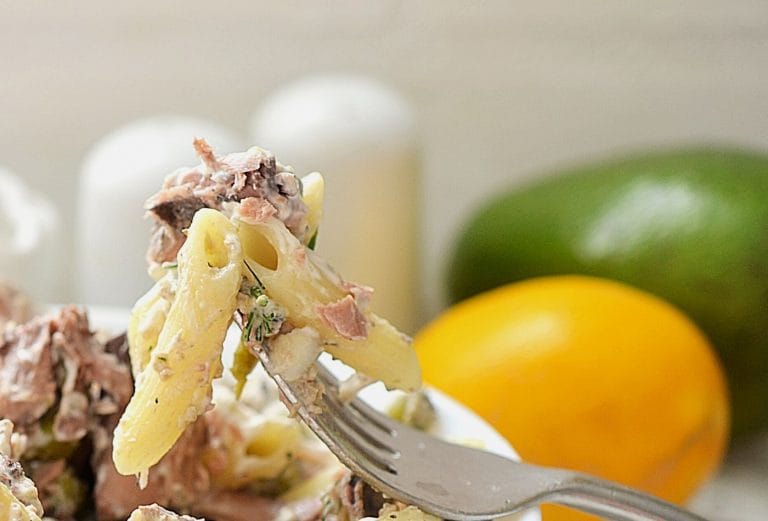 a fork full of tuna pasta salad over the bowl with citrus fruits behind