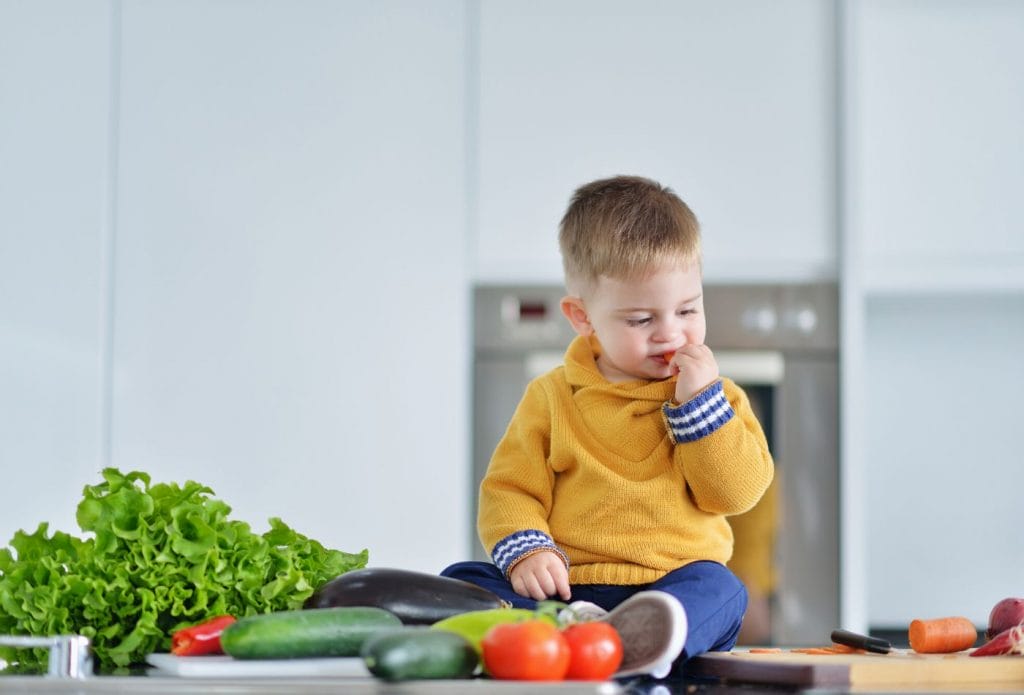 toddler boy sitting on a counter munching on vegetables and eating healthier