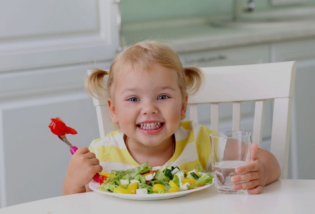 toddler girl with a fork full of veggies and a plate full of healthy food