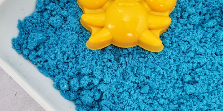 blue kinetic sand in a bin with a crab mold