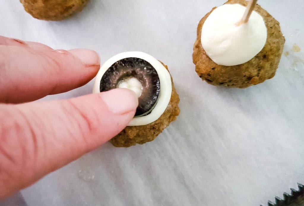 Meatball with mozzarella and an olive ring being pressed on to make an eyeball