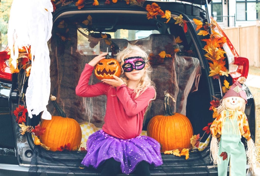 girl in a homemade halloween costume sitting in the back of a car with pumpkinds