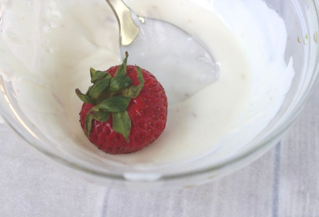 a strawberry being dipped in white chocolate