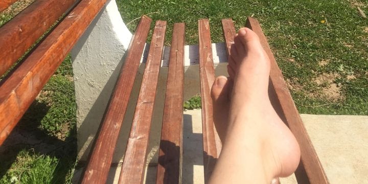 feet relaxing on a bench outside on the grass