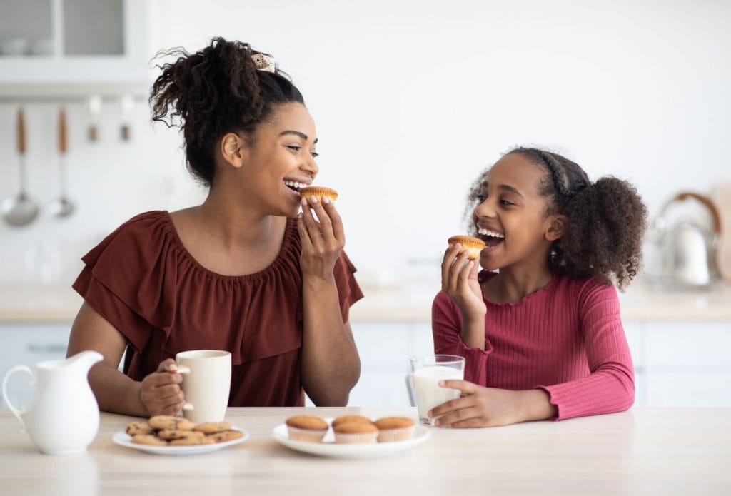 mom and grateful daughter smiling at each other eating muffins