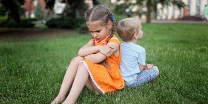 two children sitting in the grass, one is angry, one is sad