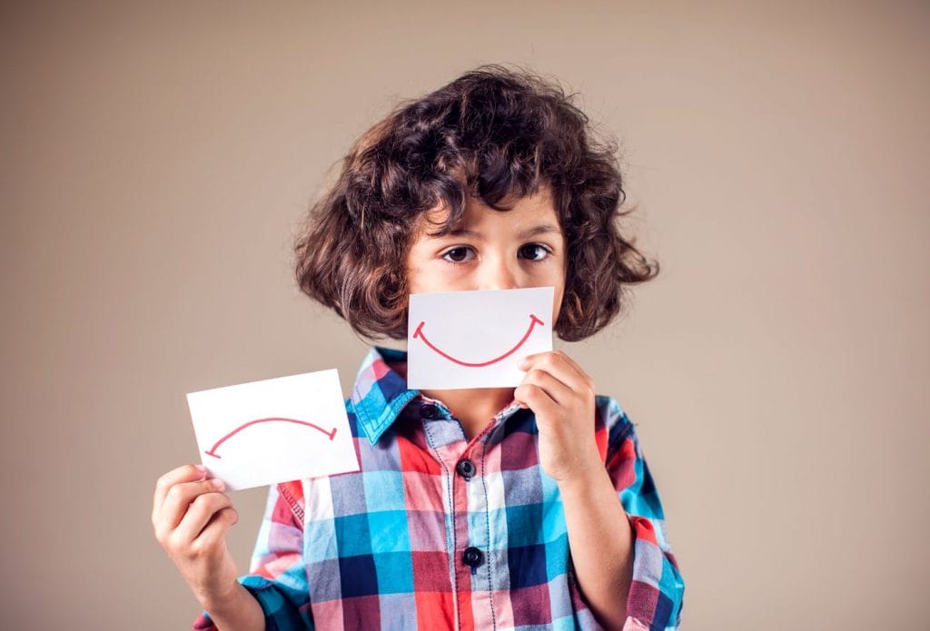 a child with smiley and frowny face cards showing emotions and showing how kids learn about emotions.