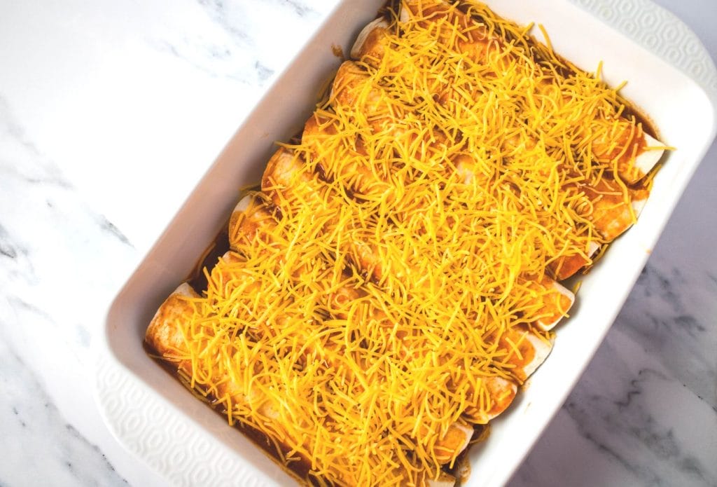 rolled leftover pork enchiladas in a pan topped with cheese ready to bake