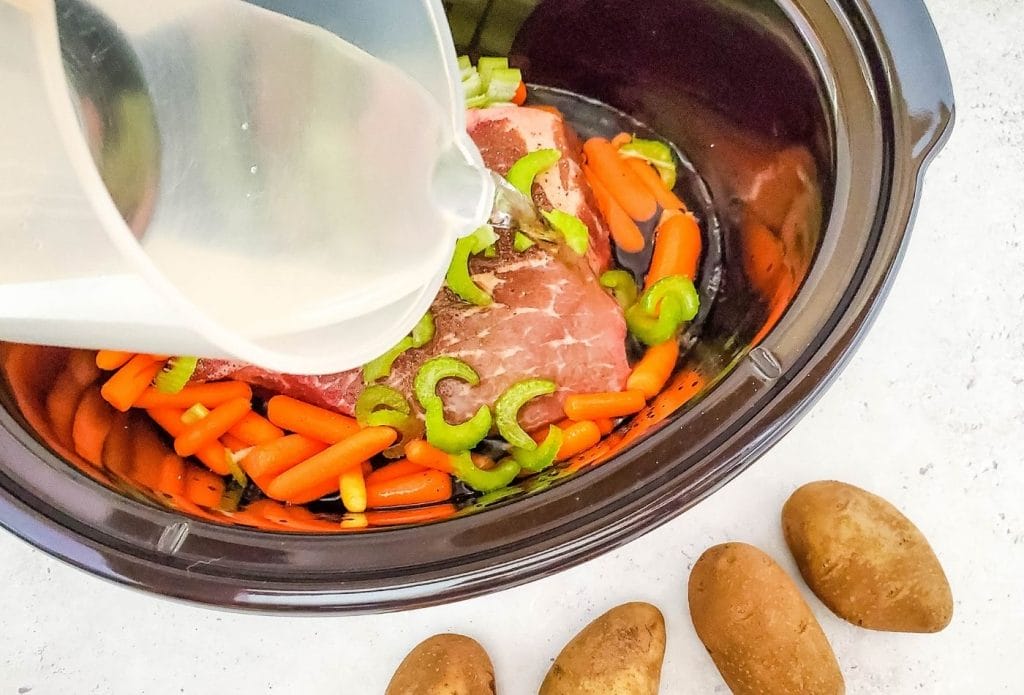 roast and vegetables going into the slow cooker