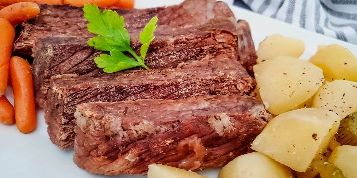 roast beef sliced on a board wtih potatoes and carrots