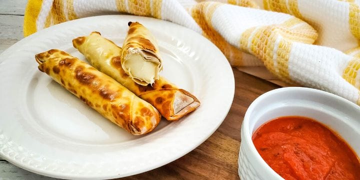 plate of air fryer mozzarella sticks next to a bowl of marinara and a yellow dish towel