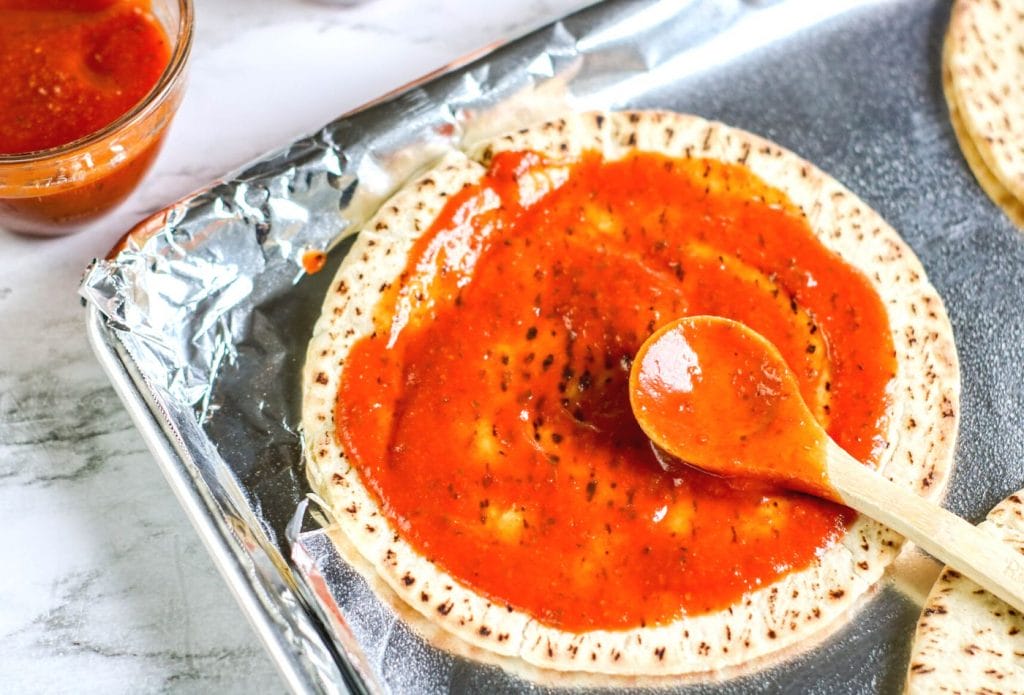 pita bread with pizza sauce being spread on