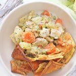 chicken pot pie stew in a bowl topped with a crispy biscuit