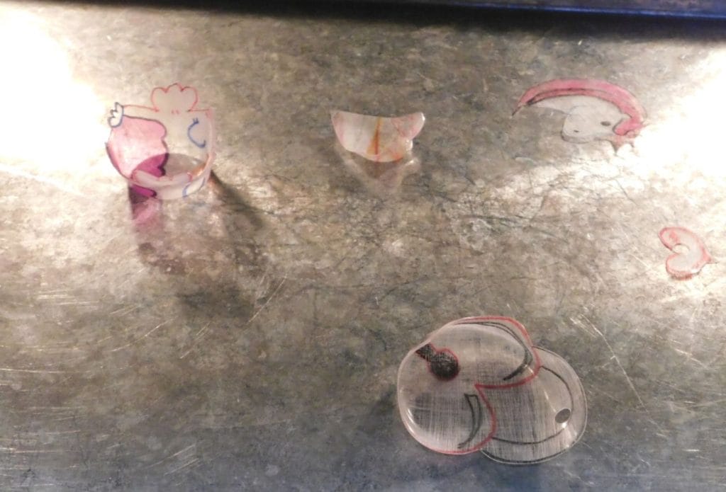 shrinky dinks shrinking in the oven on a sheet pan