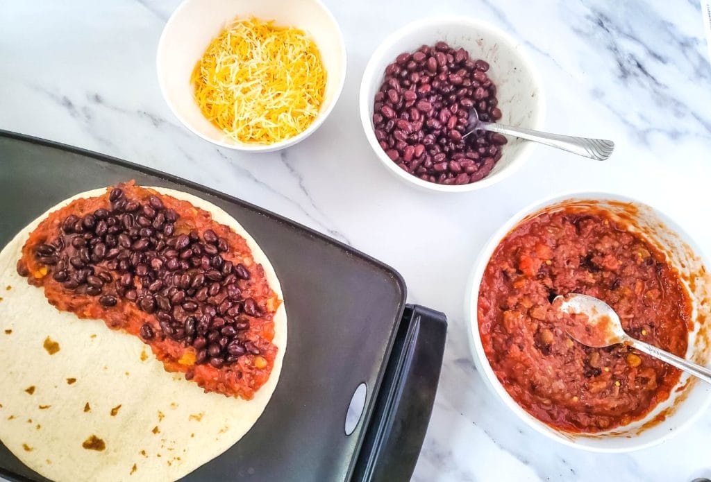 flour tortilla with rotel and black beans with bowls of rotel, black beans and shredded cheddar around them