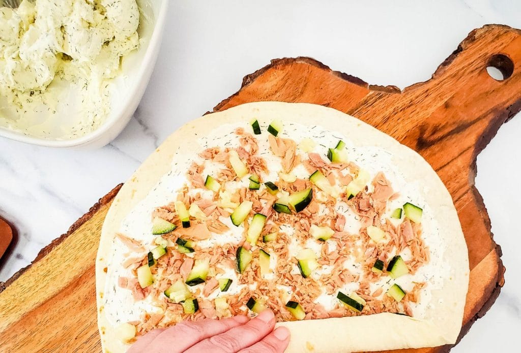 cucumbers and tuna on a tortilla being rolled up