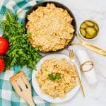 cheeseburger pasta in a skillet next to a plate full and pickles and tomatoes