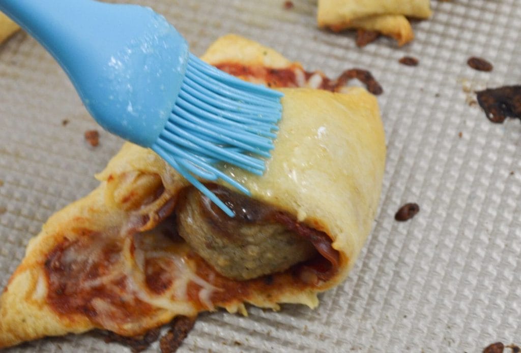 brushing butter on a pepperoni meatball roll up
