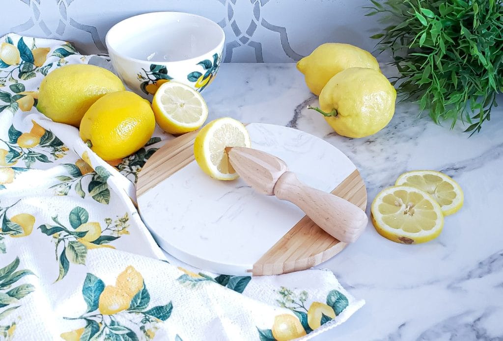 lemons on a cutting board with a lemon reamer and slices and a bowl and whole lemons