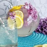 lilac lemonade on a mat with a glass and some lilac flowers