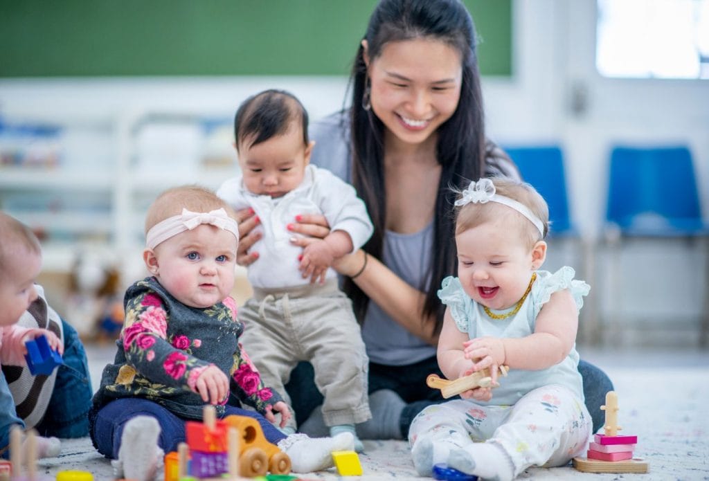 children sitting on the floor playing with daycare provider