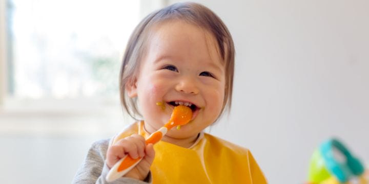 a toddler feeding herself with a spoon