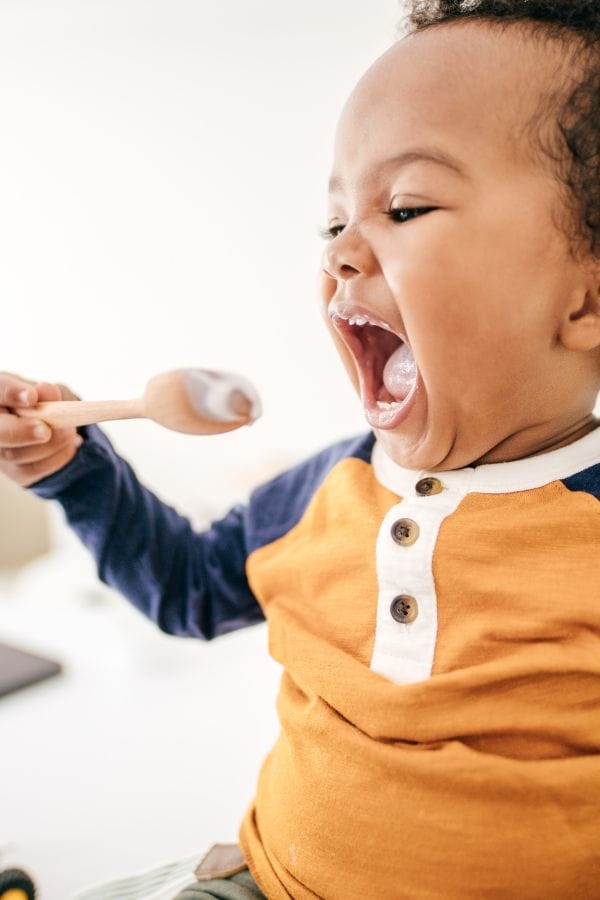 a toddler enjoying eating with a spoon