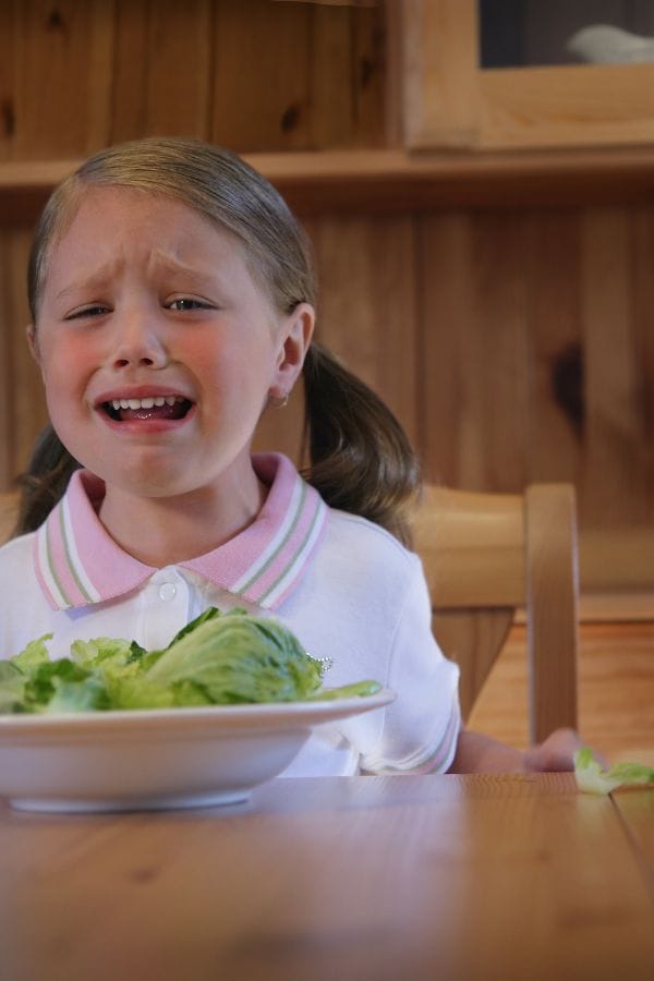 a picky toddler crying in front of a plate of vegetables