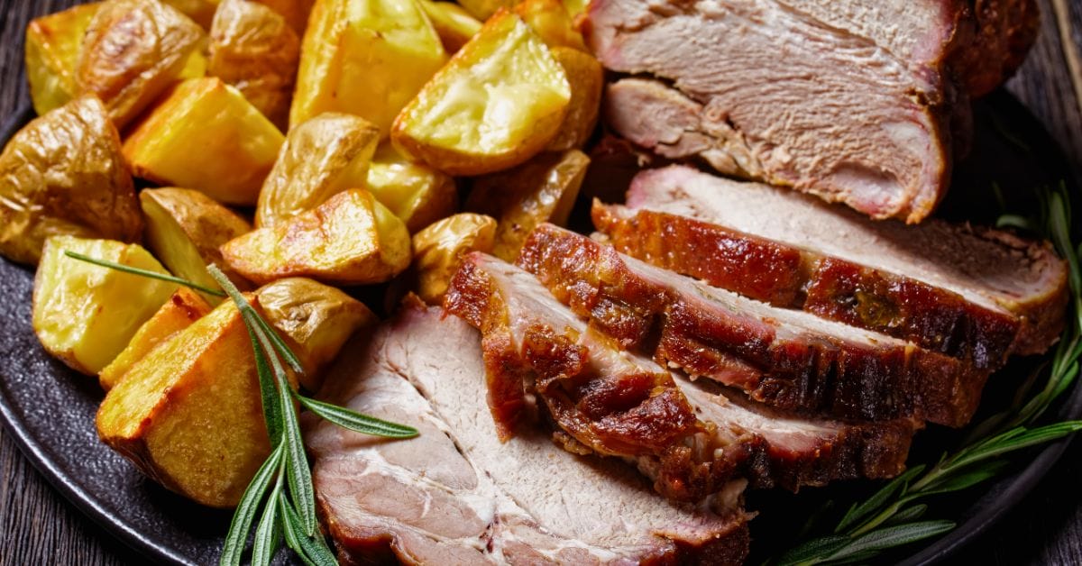 slices of pork loin on a plate with some roasted potatoes.