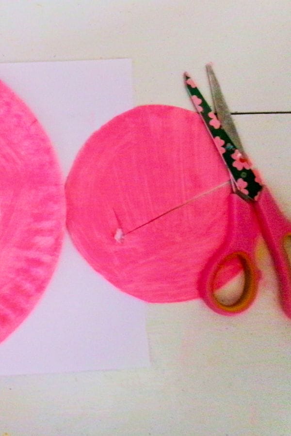 cutting the middle out of a painted paper plate to make a wreath for valentine's day