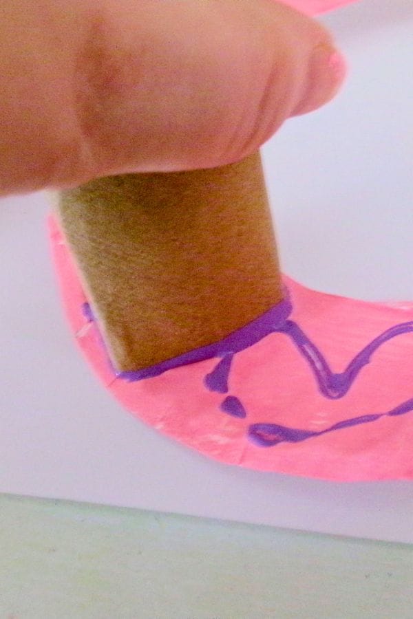 stamping painted hearts on a paper plate wreath with a toilet paper tube