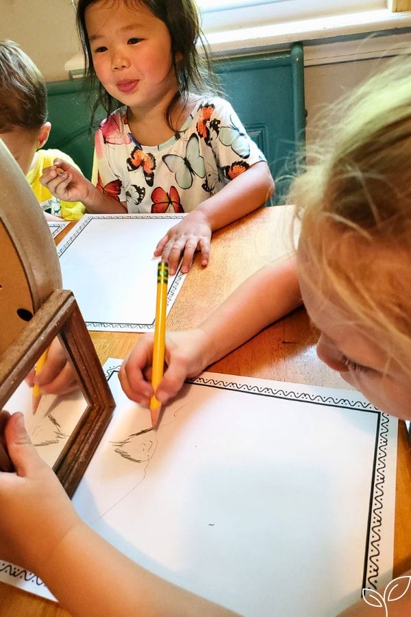 a child drawing her own likeness while she looks in the mirror