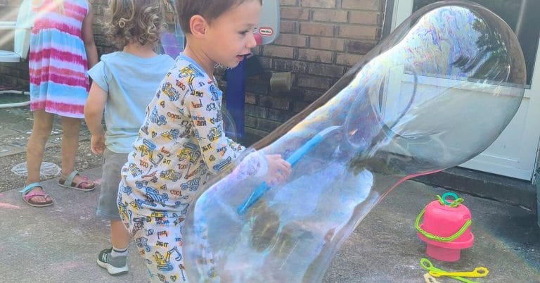 a child making a really big bubble with a bubble wand outside