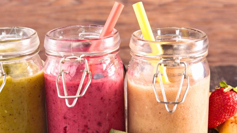different flavors of smoothies in jars with straws