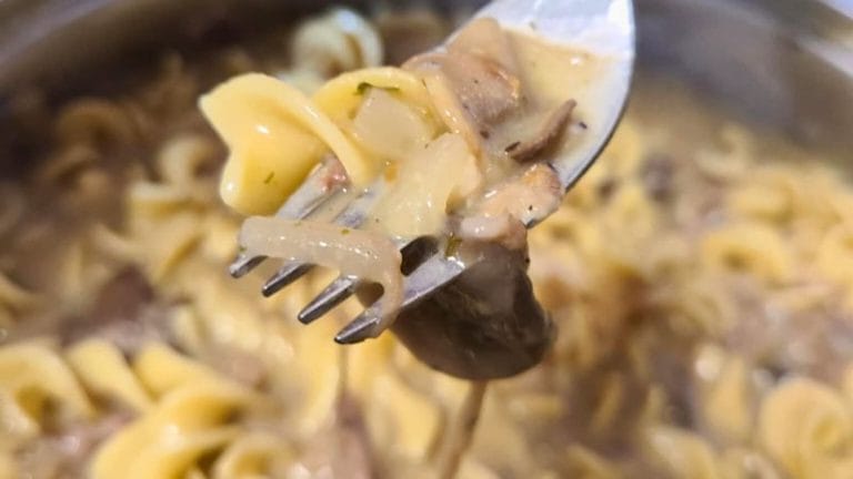 a fork full of roast pork stroganoff above a pan full