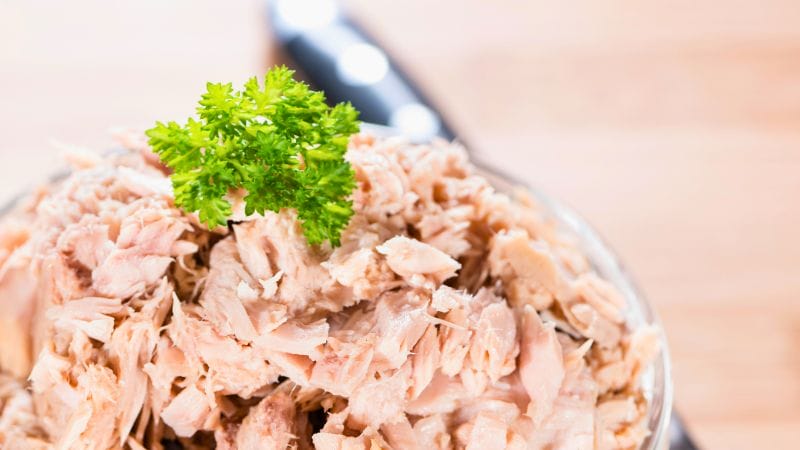 canned tuna in a bowl with a green garnish of parsley