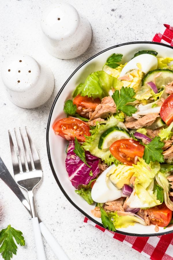 a plate with a pretty salad topped with flakes of canned tuna with a fork and salt and pepper shakers