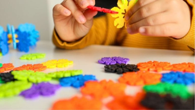 a child's hands building a structure with small plastic pieces