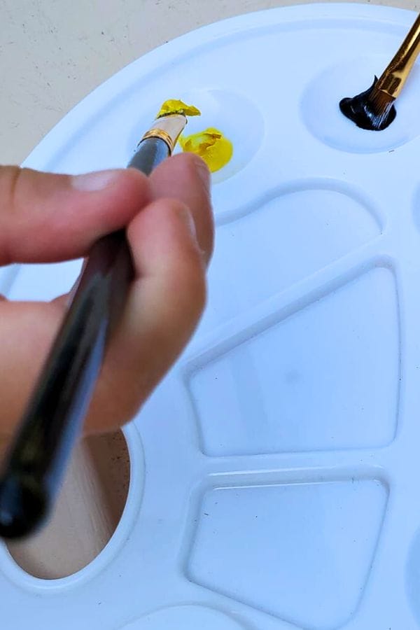 a child holding a paint brush and filling it with yellow paint
